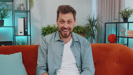 young smiling man pointing to camera, choosing lucky winner, indicating, inviting, approve at home