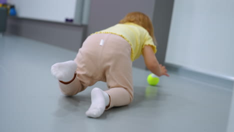 toddler holding tennis balls, one bouncing from hand, while adult rests on green exercise ball in gym, fitness environment includes purple mat, workout equipment, and modern decor