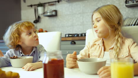 Two-Siblings-Having-Cereal-With-Milk-For-Breakfast-In-The-Kitchen