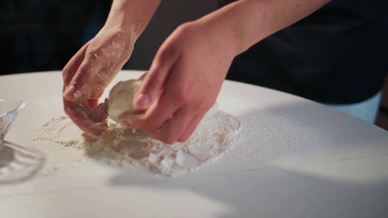 打ち粉をした表面で生地をこねる手のクローズアップ。食べ物を準備する間、人は集中し慎重です。レシピ、ベーキングチュートリアル、またはレストランのプロモーションに最適です。