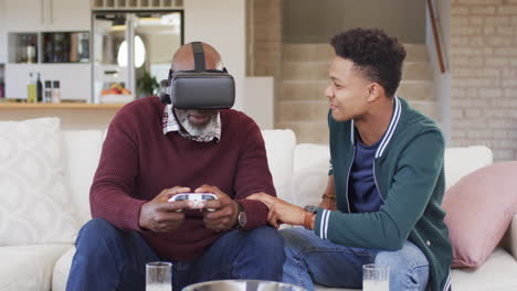 Happy-african-american-father-using-vr-headset-and-gamepad-with-adult-son-at-home,-slow-motion