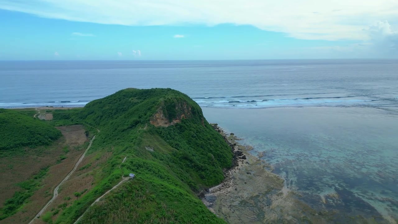 Vista della costa dell'isola di Lombok che mostra lussureggianti colline verdi, un sentiero tortuoso, onde oceaniche distanti e acqua limpida e poco profonda. Splendida vista aerea con speed ramp, hyper motion, time lapse, ampio panorama orbitale
