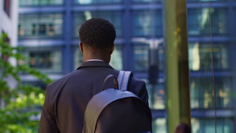 rear view of businessman wearing backpack walking to work in offices in the financial district of the city of london uk 1