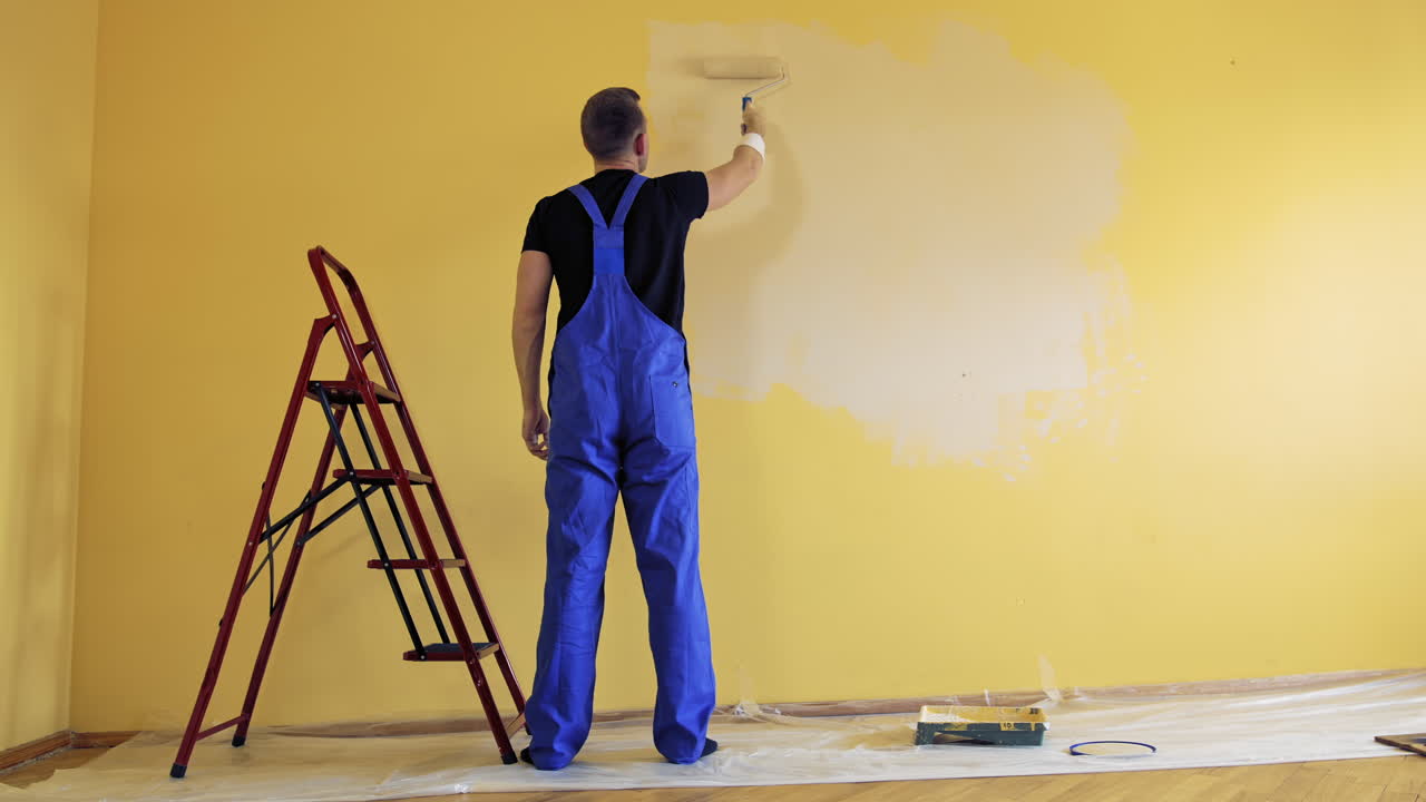 Painter paints on yellow wall. Repair, building and home concept.