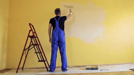 painter paints on yellow wall. repair, building and home concept.