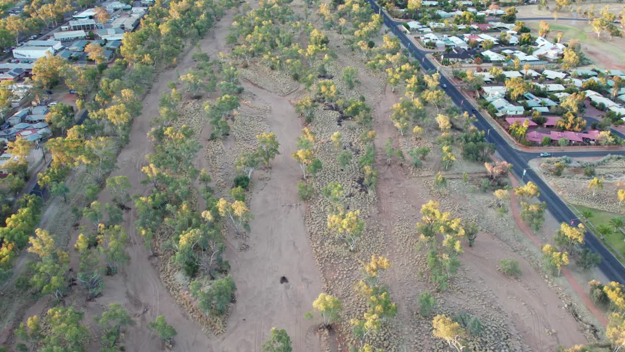Aerial footage moving forward along the Todd RIver showing houses and roads alongside, in the late afternoon. Alice Springs, Mparntwe, Northern Territory, Australia. August 2022.