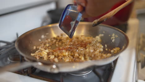 adding a liquid and tomato paste to a pan full of fried onions and meat for a homemade recipe