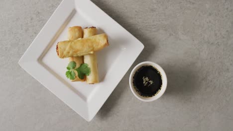 composition of plate with spring rolls and soy sauce on grey background