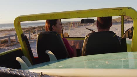 feliz pareja caucásica sentada en un buggy de playa junto al mar hablando