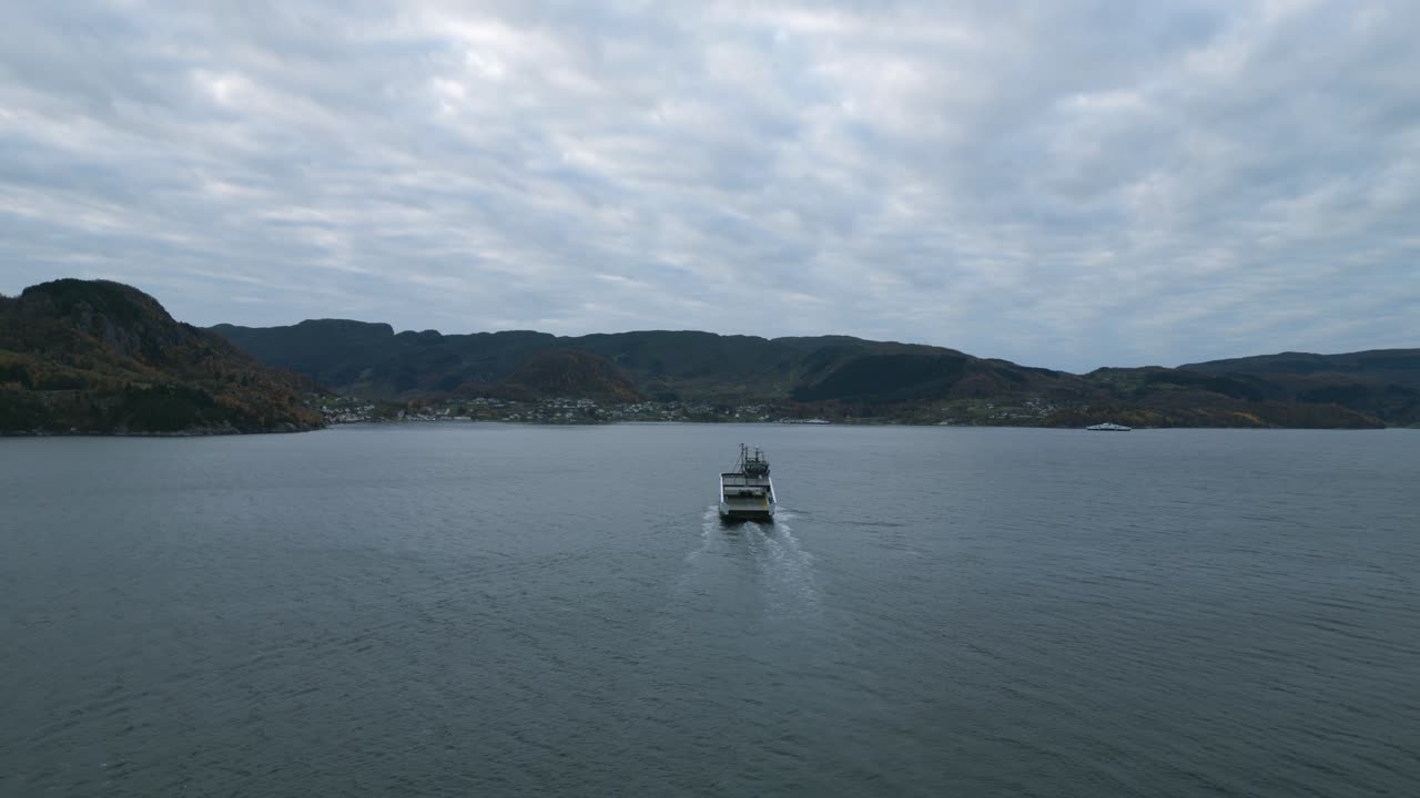 un ferry cruzando aguas tranquilas cerca de nesvik con el telón de fondo de hjelmeland, cielos nublados, vista aérea