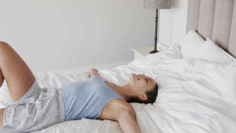 Portrait-of-happy-biracial-woman-lying-on-bed-at-home,-slow-motion