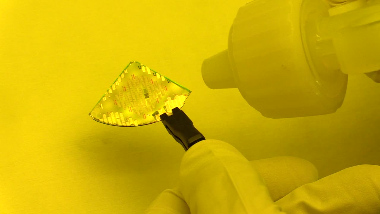 Close-up view of a silicon wafer being handled with tweezers in a cleanroom environment
