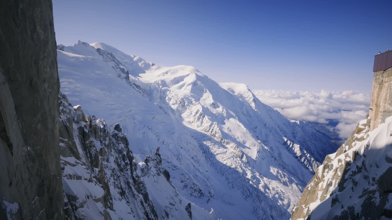 View of Mont Blanc from the Aiguille du Midi at midday. The snow-capped peaks glisten in the intense light, offering a majestic Alpine panorama and a total immersion in the grandeur of the Alps.