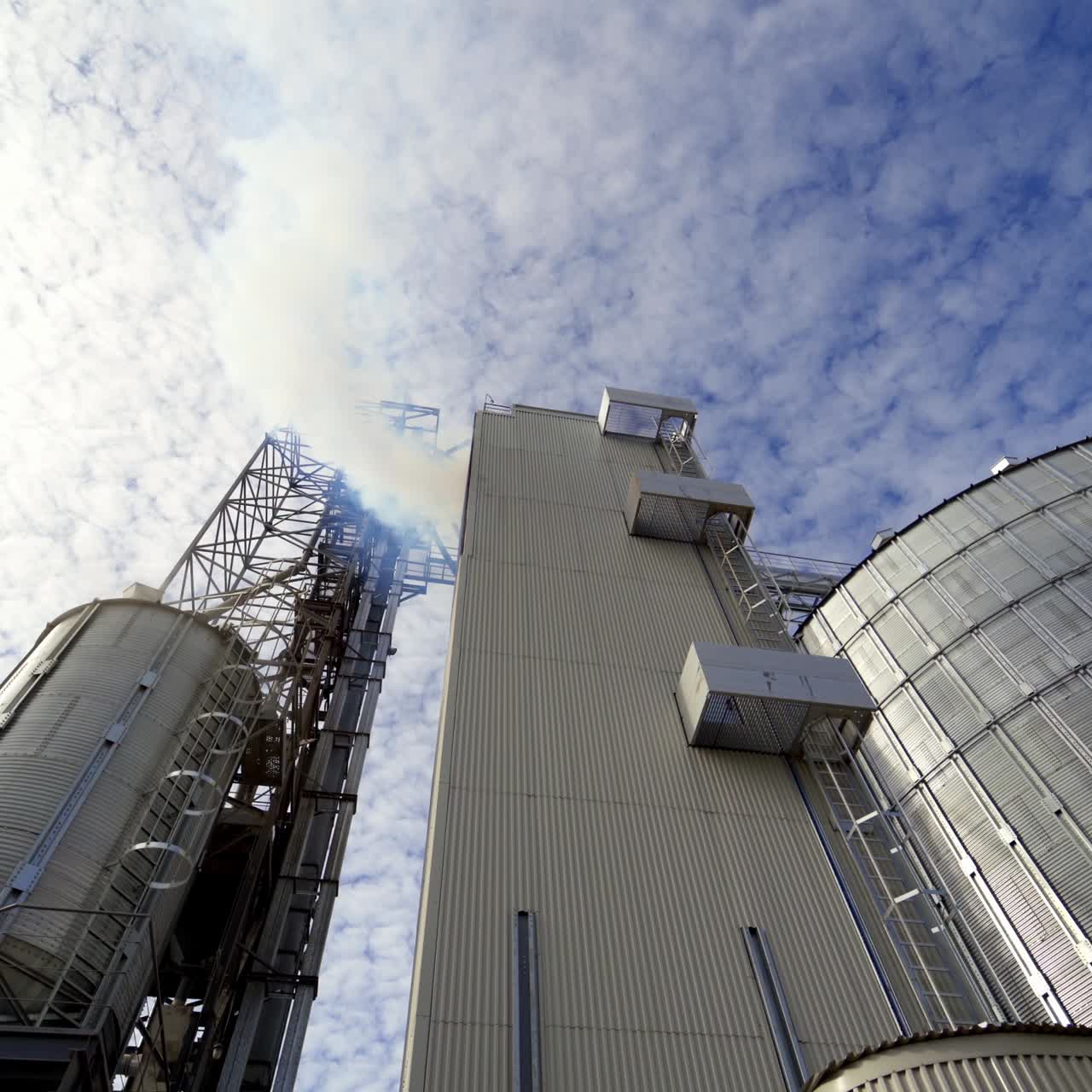 Modern warehouse. Grain elevator outdoors. Agricultural complex for grain processing. White fumes go from the industrial plant. View from below.