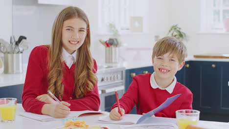 Retrato-De-Hermano-Y-Hermana-Vistiendo-Uniforme-Escolar-Haciendo-La-Tarea-En-La-Cocina