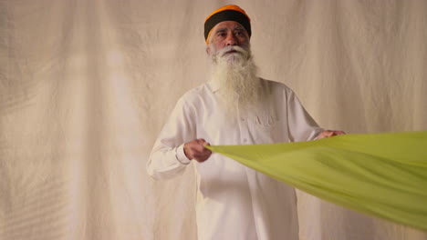 fotografía de estudio de un anciano sikh doblando tela para un turbante contra un fondo plano como secuencia parte 2 de 2