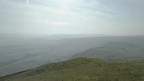 Drone-shot-from-the-top-of-Mam-Tor-moving-towards-the-valley-of-where-Castleton-resides,-Peak-District-showing-the-valley-and-mountains