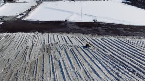 Quitanieves-Amarillo-Limpiando-Un-Enorme-Campo-De-Nieve,-Invierno,-Ciudad-De-Ottawa,-Amplia-Antena-De-Establecimiento