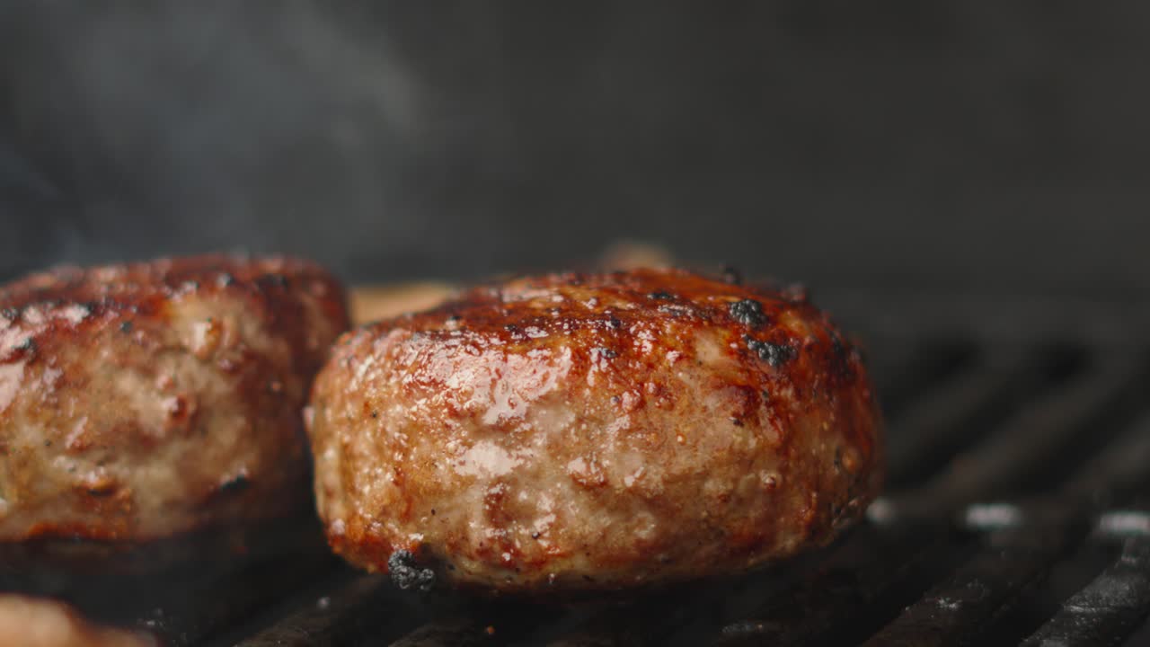 Close Up of Delicious Juicy Beef Quarter Pounder Burger Patties on Hot BBQ Iron Grill with Smoke Rising in Slow Motion. High Protein Tasty Unhealthy Summer Food