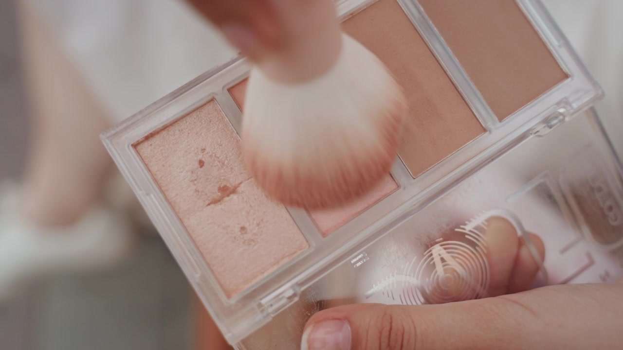 Mano tiene pennello e palette per il trucco, dimostrando l'applicazione di varie tonalità. Una vista ravvicinata evidenzia diversi prodotti cosmetici in tonalità pastello mentre vengono campionati con illuminazione soffusa