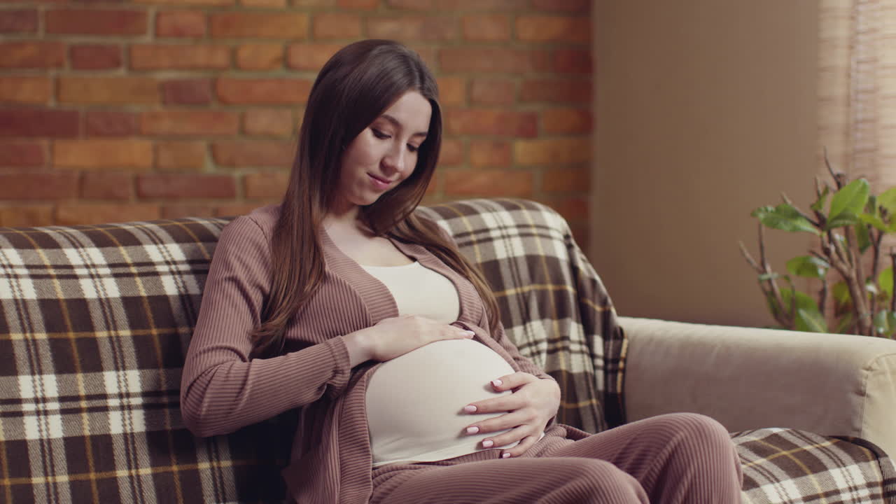 임신 한 여자 가 소파 에 앉아 배 를 만지고 있다