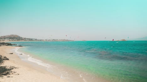 Zeitraffer-Eines-Tropischen-Strandes-Auf-Einer-Griechischen-Insel-Mit-Gleitschirmfliegern,-Die-Im-Hintergrund-Extremsport-Betreiben