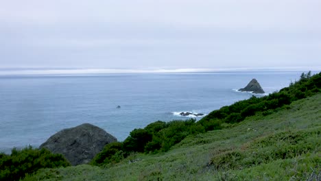 a small fishing boat goes across the pacific ocean in the distance by a rock island