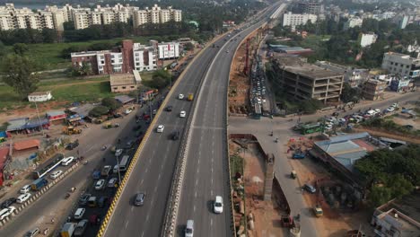 Indian-Highway-Es-Una-Filmación-Aérea-Cinematográfica-De-Automóviles-En-Rápido-Movimiento-Y-La-Construcción-De-Un-Puente-De-Metro-Visible-Sobre-Las-Vías-De-Servicio.