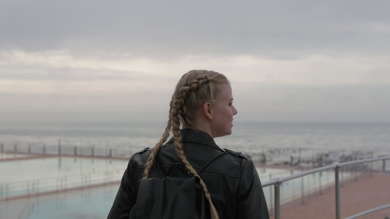 retrato de una mujer joven con el pelo trenzado sonriendo esperando a la orilla del mar con una chaqueta de cuero