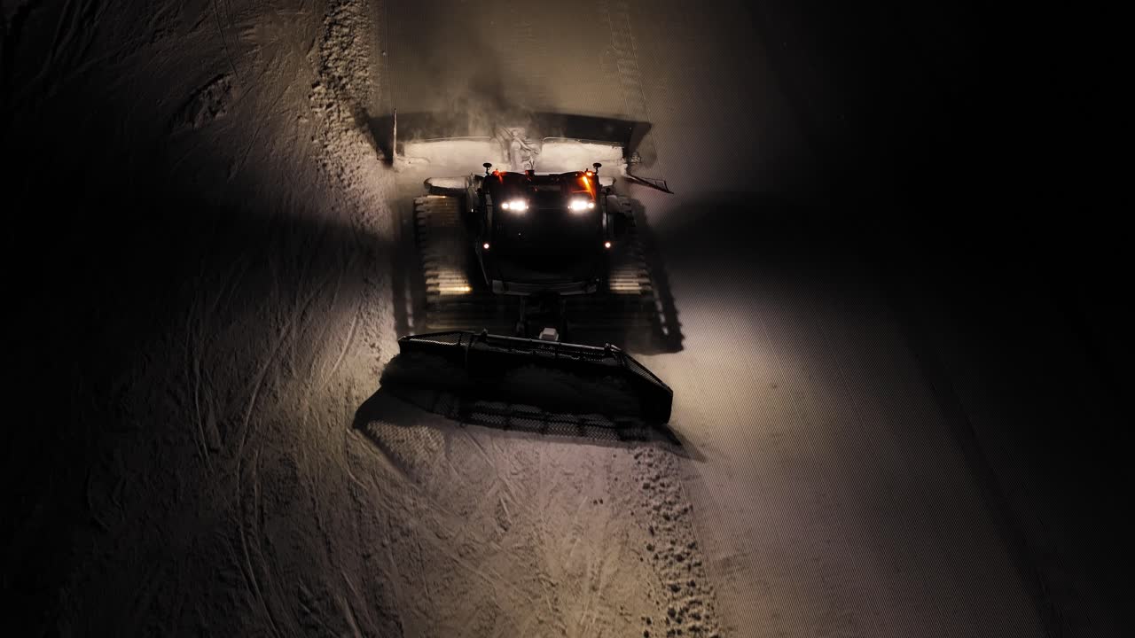 Gatto delle nevi al lavoro di notte nelle Dolomiti, bagliore alpino sulla neve, vista dall'alto