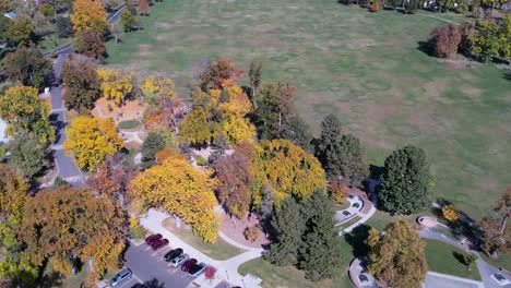 a 4k drone shot over washington park, with the denver city skyline and the rocky mountain foothills in the distance, during the colorful fall season in colorado