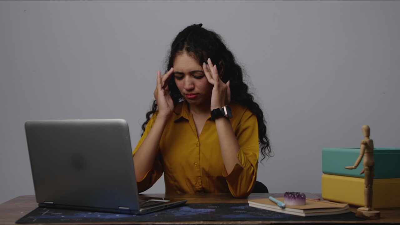 A south Asian woman massaging her head at her desk in an office, taking a brief moment to relax and relieve mental tension during work