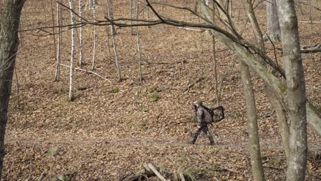 side view of bowhunter holding hunting equipment walking on winter forest path