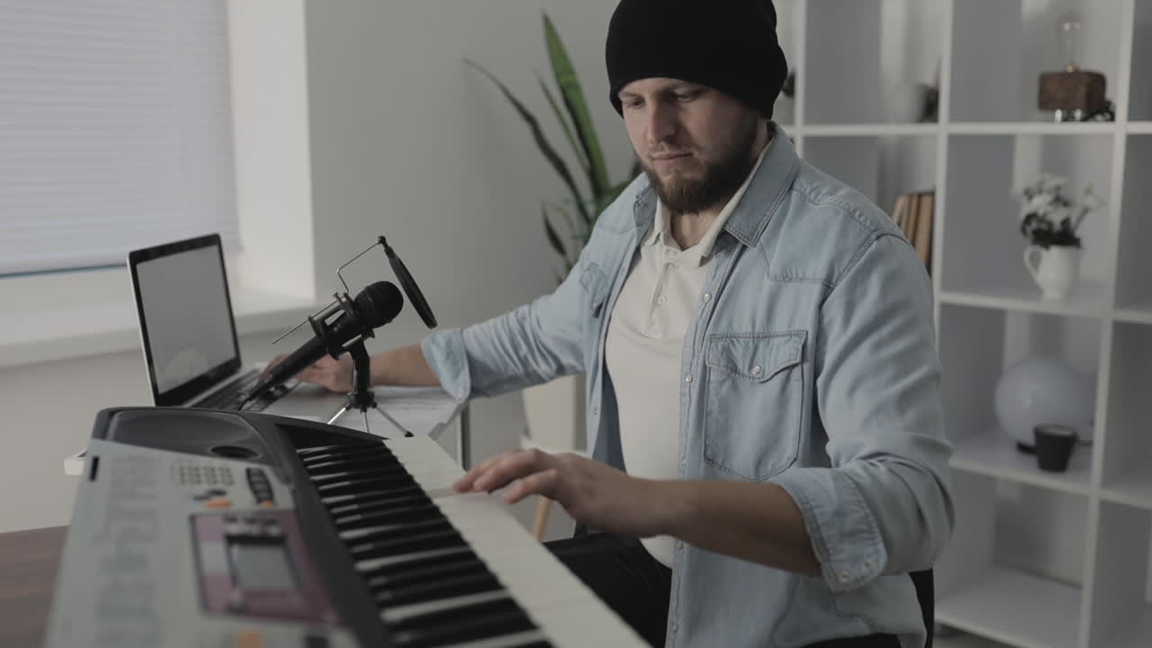 músico masculino tocando teclado eléctrico y usando una laptop en casa 1