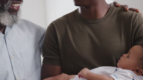 proud grandfather with adult son cuddling baby grandson in nursery at home