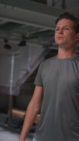 vertical video portrait of determined male athlete sport training in gym standing and warming up in changing room with focused expression