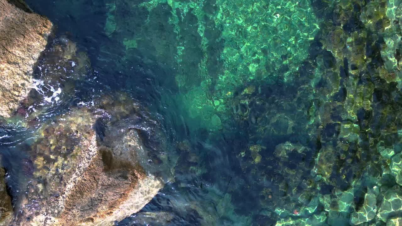 Transparent turquoise water flows between rocks in a bay in Ibiza, Spain. Breathtaking aerial view flight vertical bird's eye view drone
