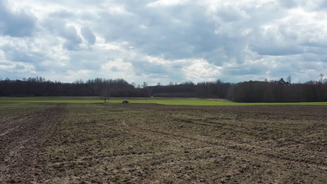 Flug über braunem Ackerland, Traktor fährt in der Ferne nahe grünem Weizen