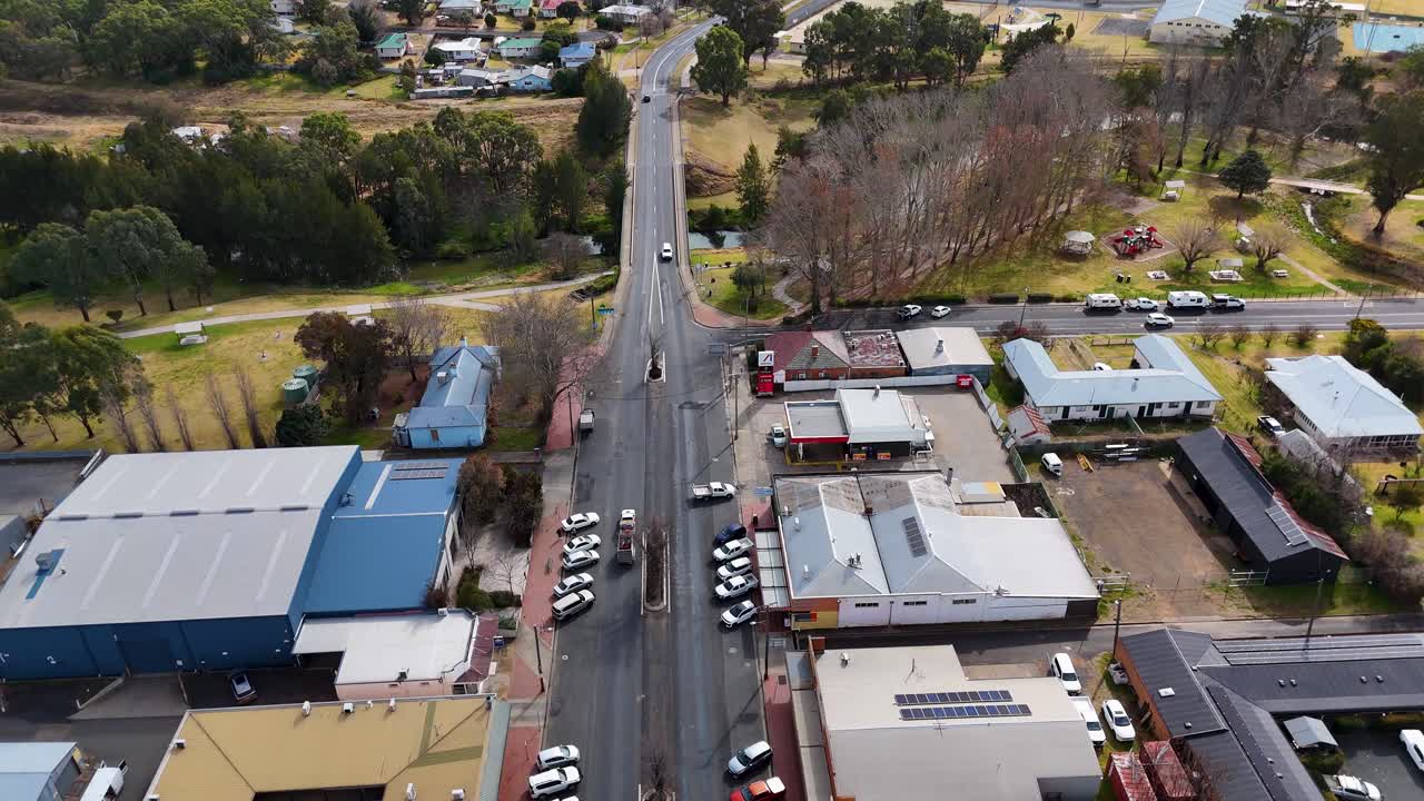 Aerial drone footage smoothly tracks over a road bridge crossing a riverbank in a small residential area, under bright natural daylight