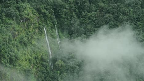 aerial view of waterfall in clouds in mountain forest, beautiful green nature shot of elevated aerial view of waterfalls in himalaya mountains in nepal in lush greenery forest scenery