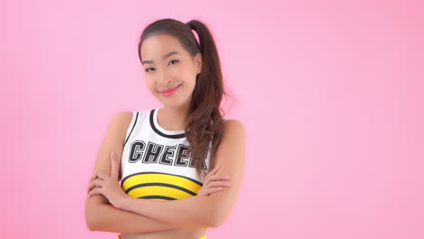 a medium close-up of a cute cheerleader smiling with her arms crossed in front of her