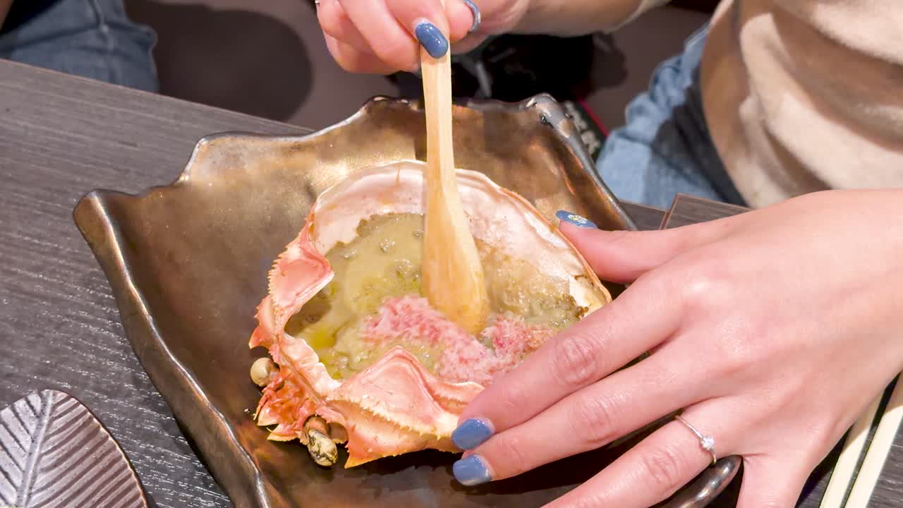 Primo piano delle mani che usano un cucchiaio di legno per mangiare miso di granchio a Tokyo