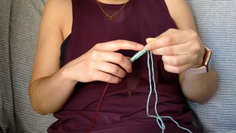 torso of a female sitting on a couch doing knitting with wool