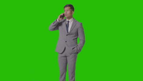 three quarter length studio shot of smiling businessman in suit talking on mobile phone against green screen 2