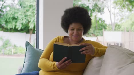 Video-of-happy-plus-size-african-american-woman-lying-on-sofa-and-reading-book