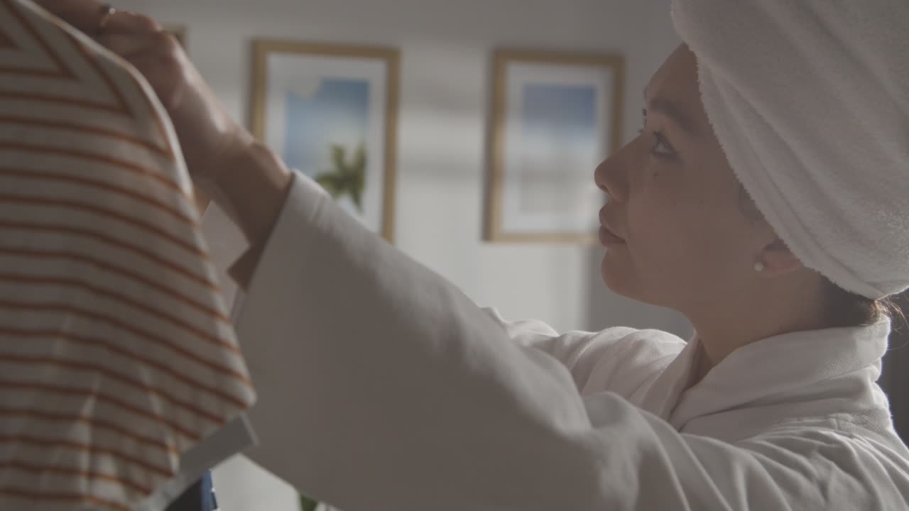 Young Woman At Home Just Out Of Shower Choosing Business Suit From Clothes Rail For Job Interview 