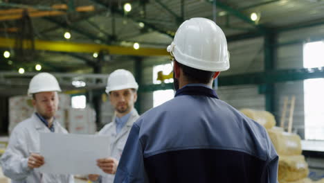 rear view of the male factory worker wearing a helmet and approaching two coworkers