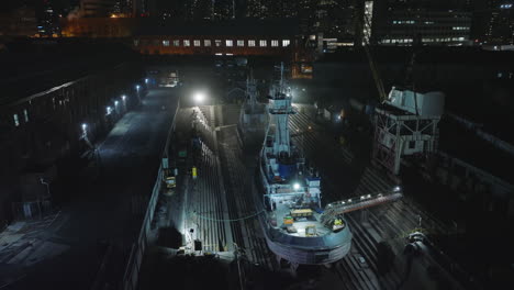 Aerial-footage-of-ships-in-repair-facility.-Dockyard-in-city-at-night.-Intensive-lights-illuminating-vessels.-Manhattan,-New-York-City,-USA