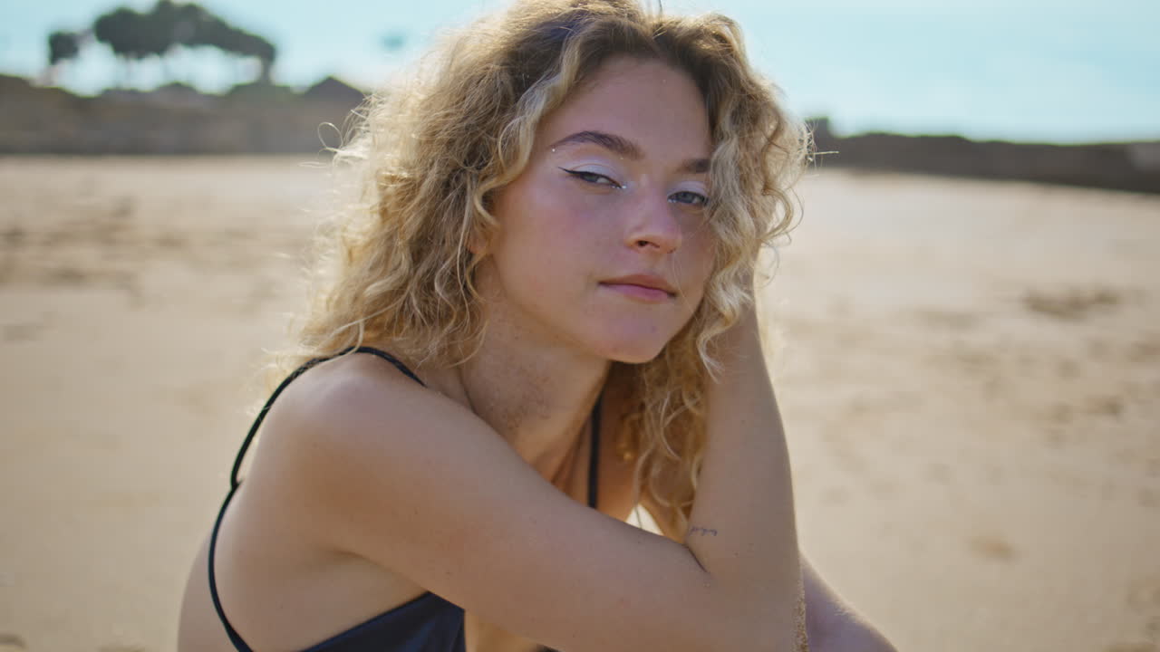 Ragazza attraente che riposa in riva al mare, guardando la telecamera in primo piano. Donna seduta sulla sabbia.