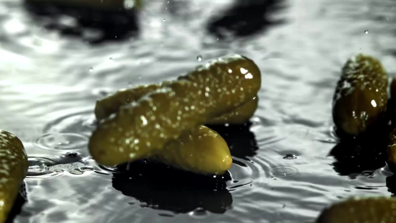 Sylteagurker som faller og plasker ned i vann i sakte film